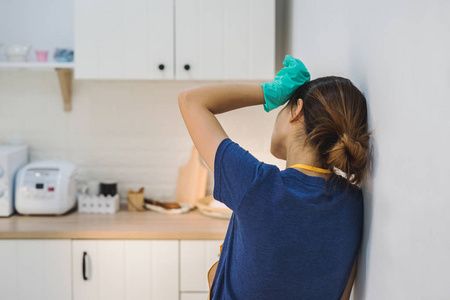 疲惫的年轻女子站在厨房房间里用清洁产品和设备, 家务观念照片